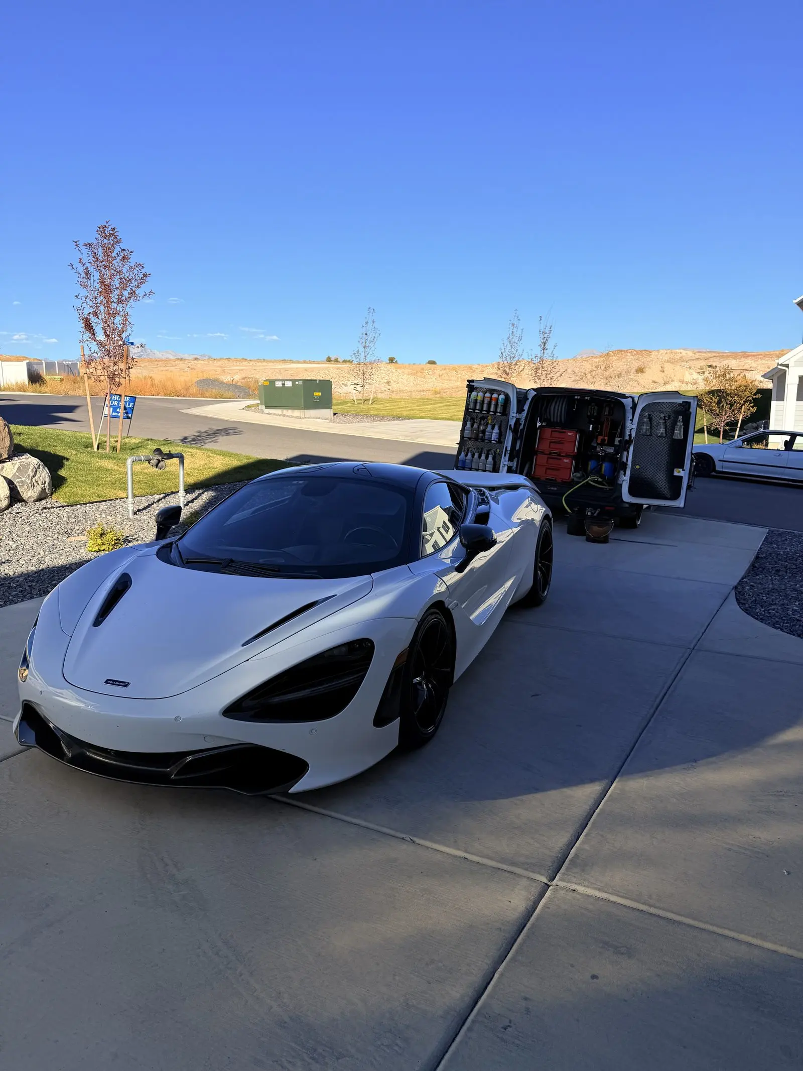 A white McLaren 720S beside the mobile detailing trailer on a client driveway