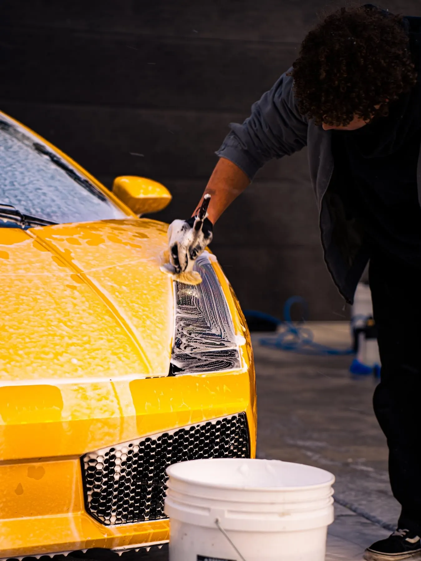 A technician working wash foam across the hood of a yellow Lamborghini by hand