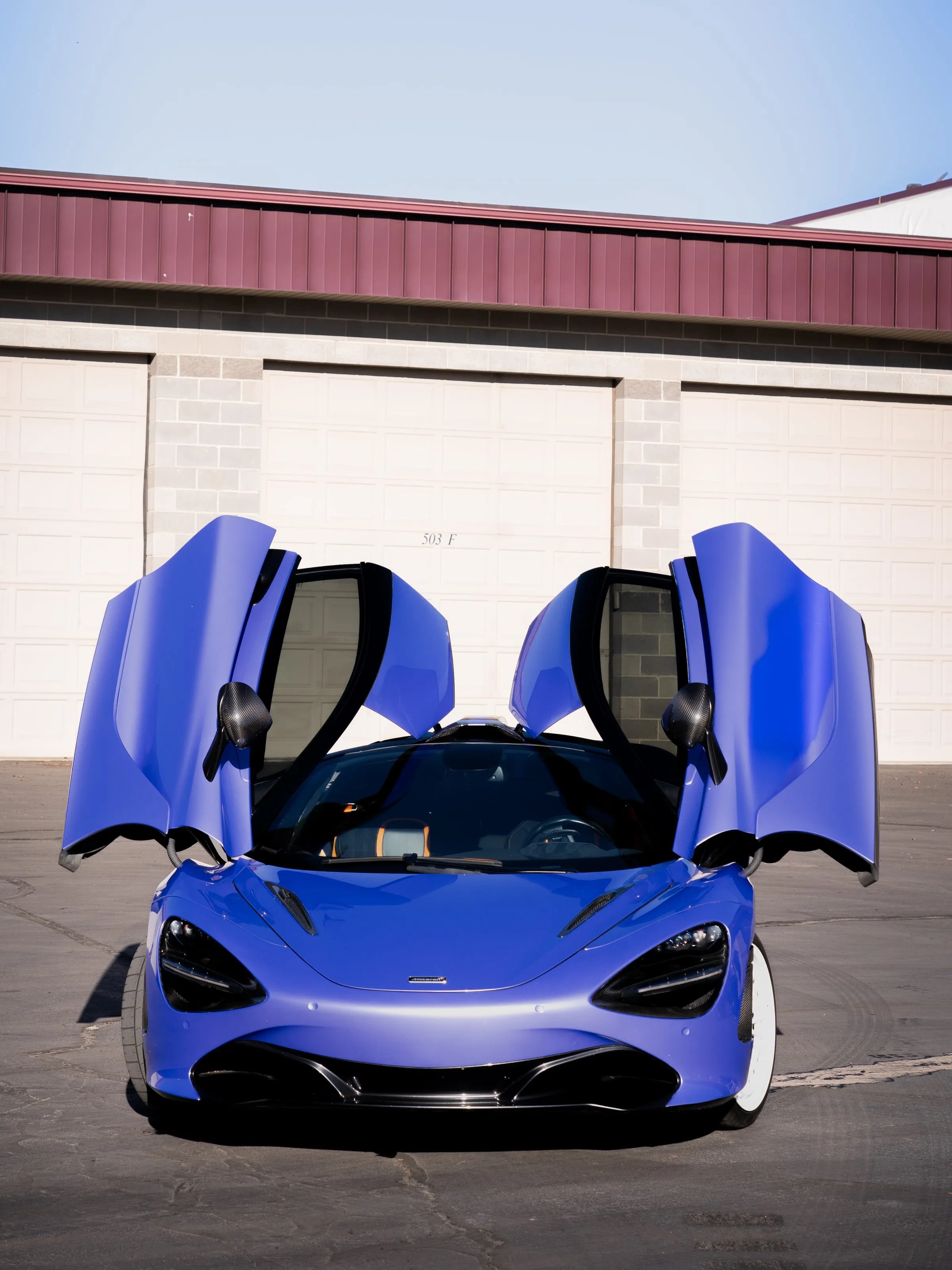 A blue McLaren 765LT with both doors up, detailed and glossy at the shop