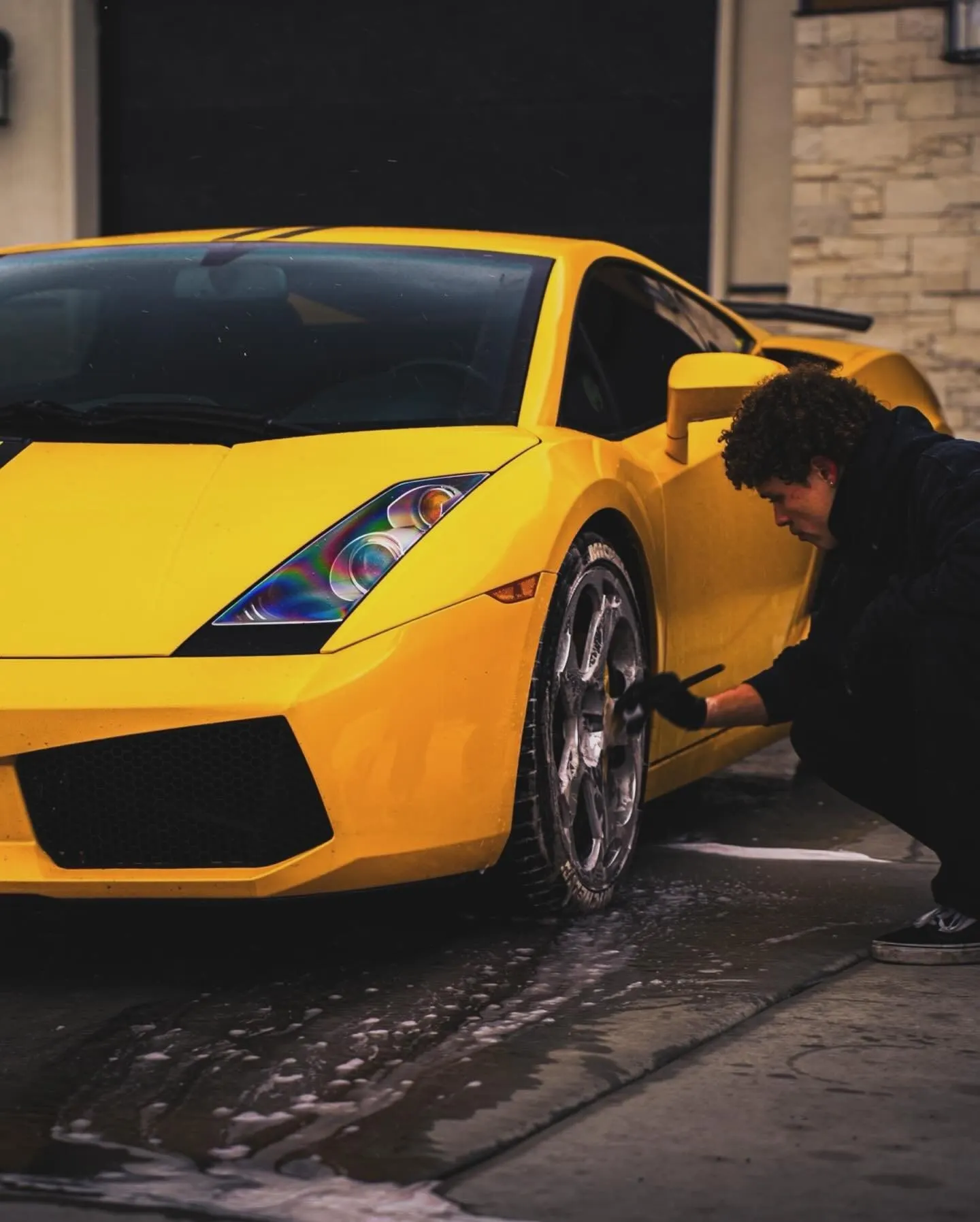 A technician hand-finishing the wheel arch of a yellow Lamborghini Gallardo