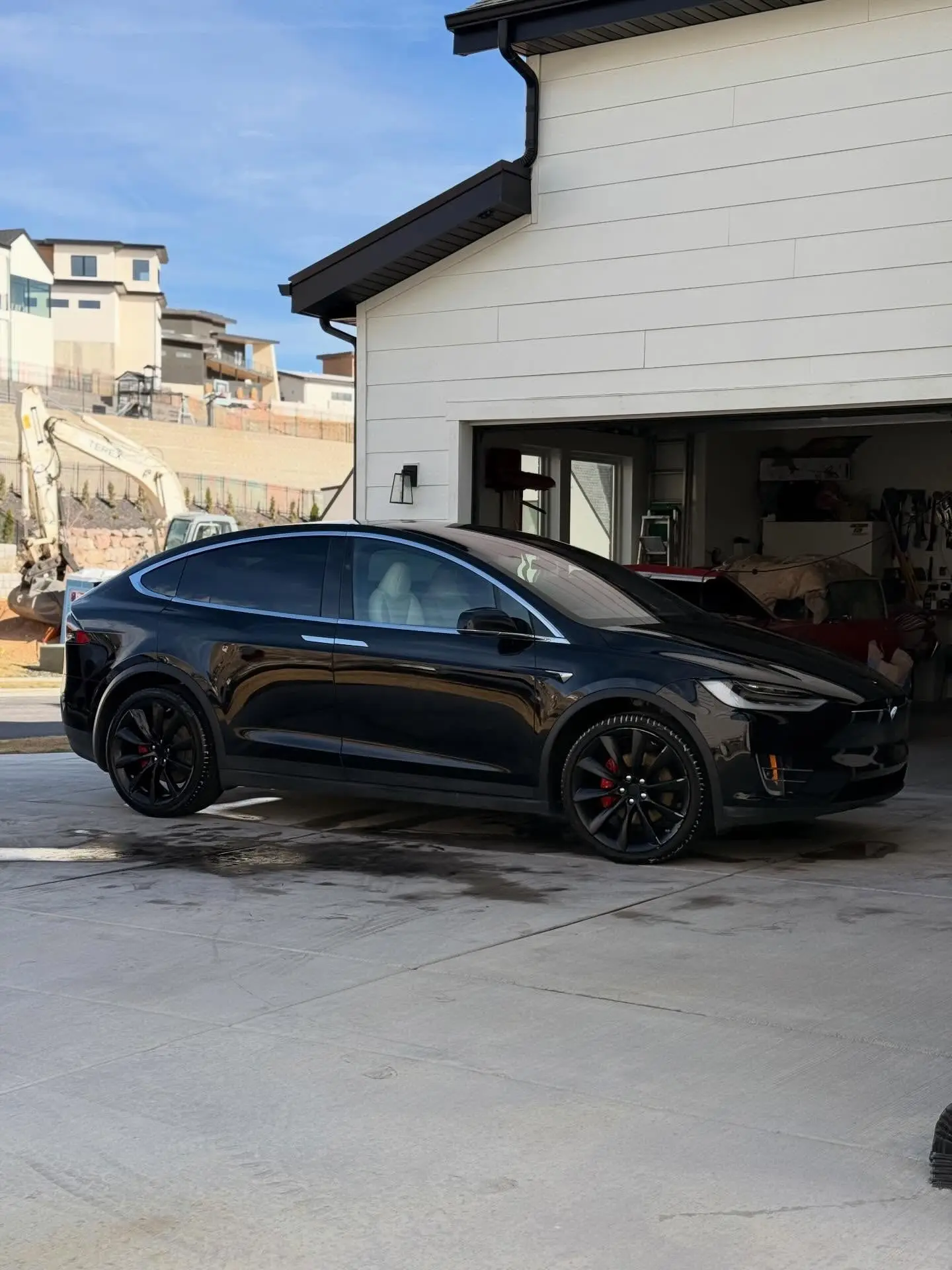 A black Tesla Model X outside a new-build home with an excavator behind
