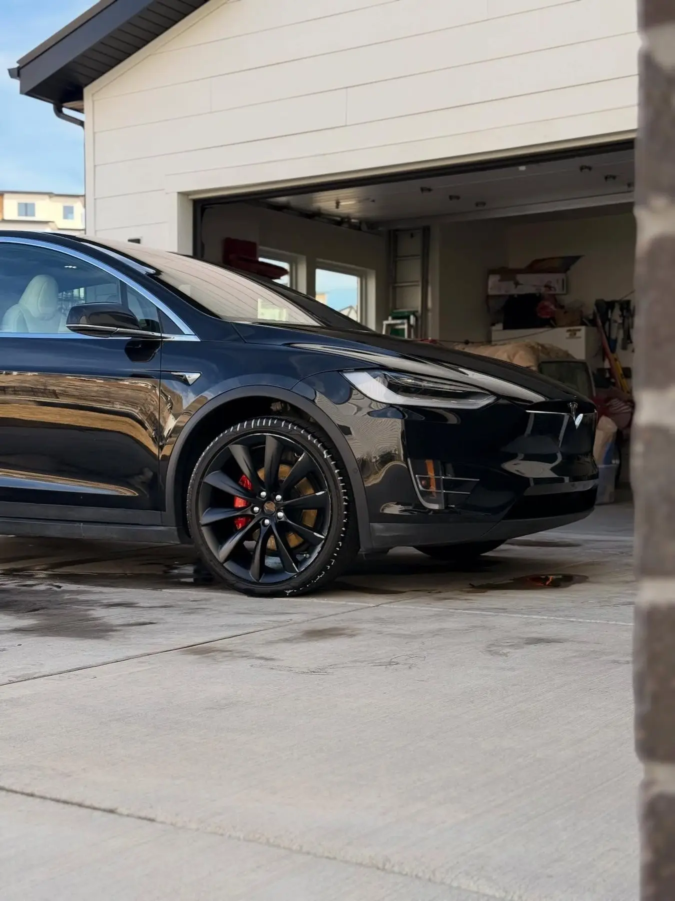 A black Tesla Model X in a home driveway after a wash