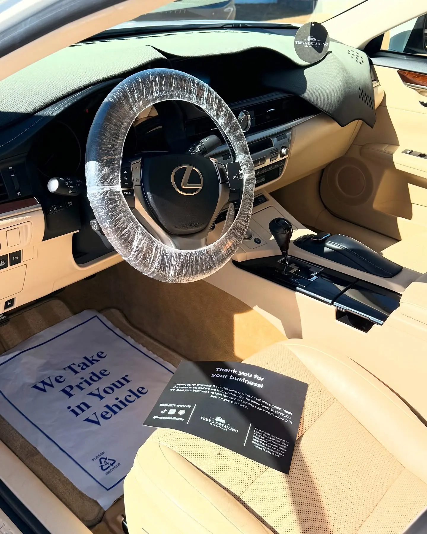 The tan interior of a Lexus ES through the open door, a wrapped wheel and care card on the seat