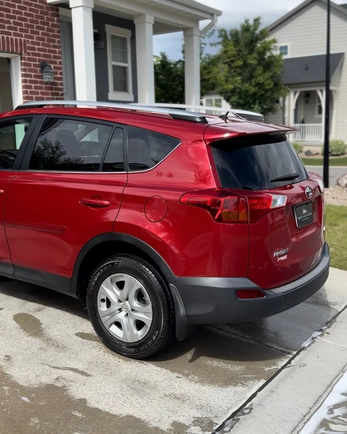 A red Toyota RAV4 rear three-quarter at a client home, freshly washed