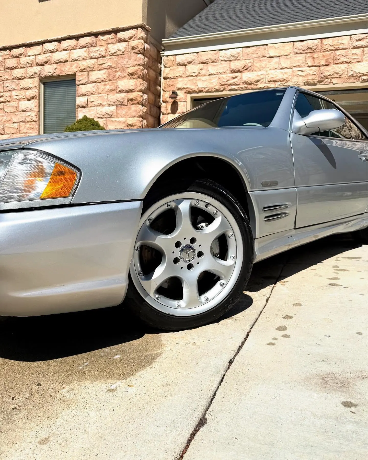 The front wheel and fender of a silver Mercedes SL500 in a driveway after detailing