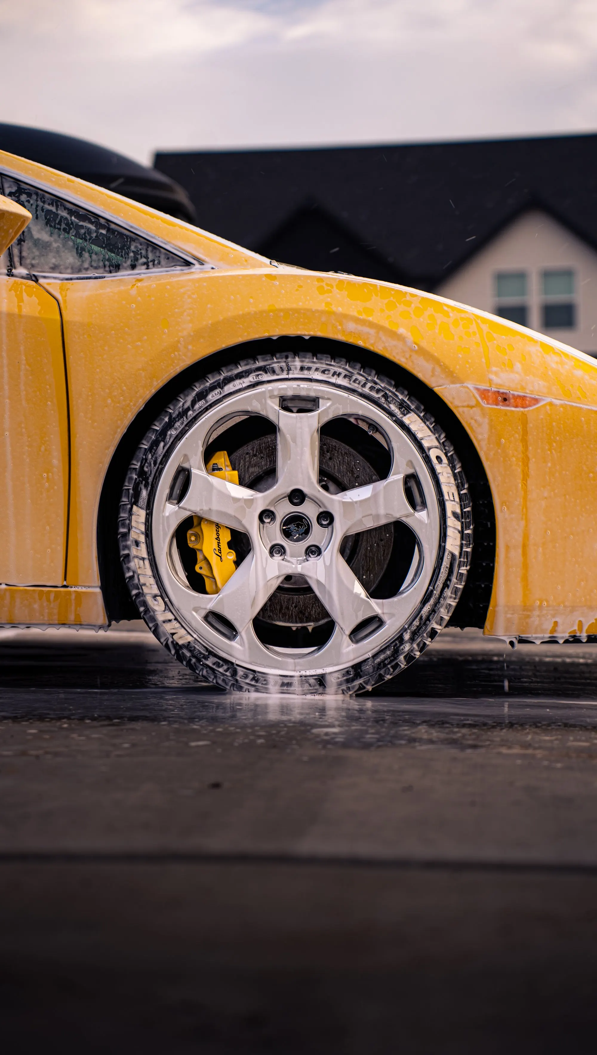A yellow Lamborghini wheel covered in wash suds, up close