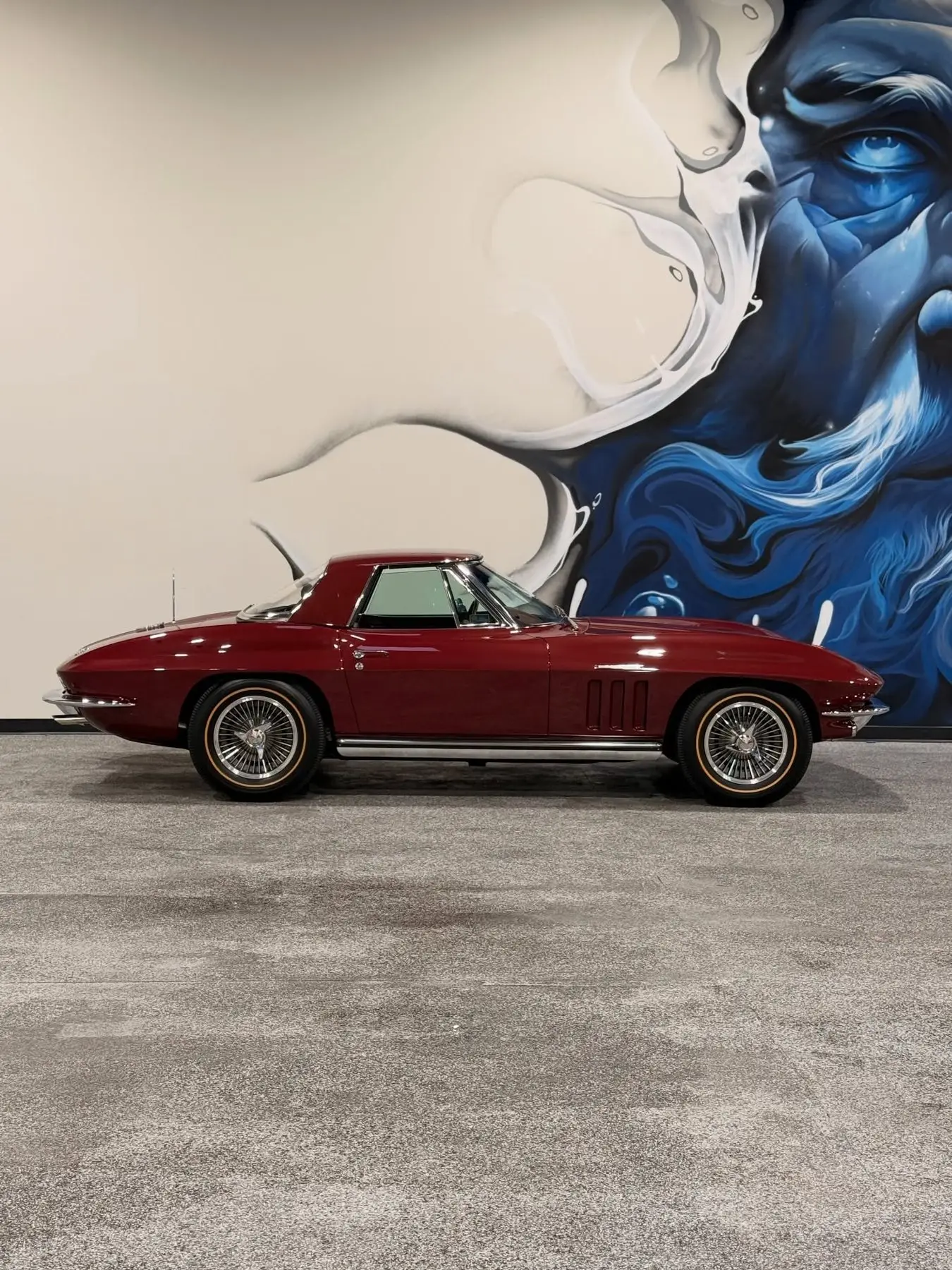A maroon Corvette Stingray parked against a painted mural