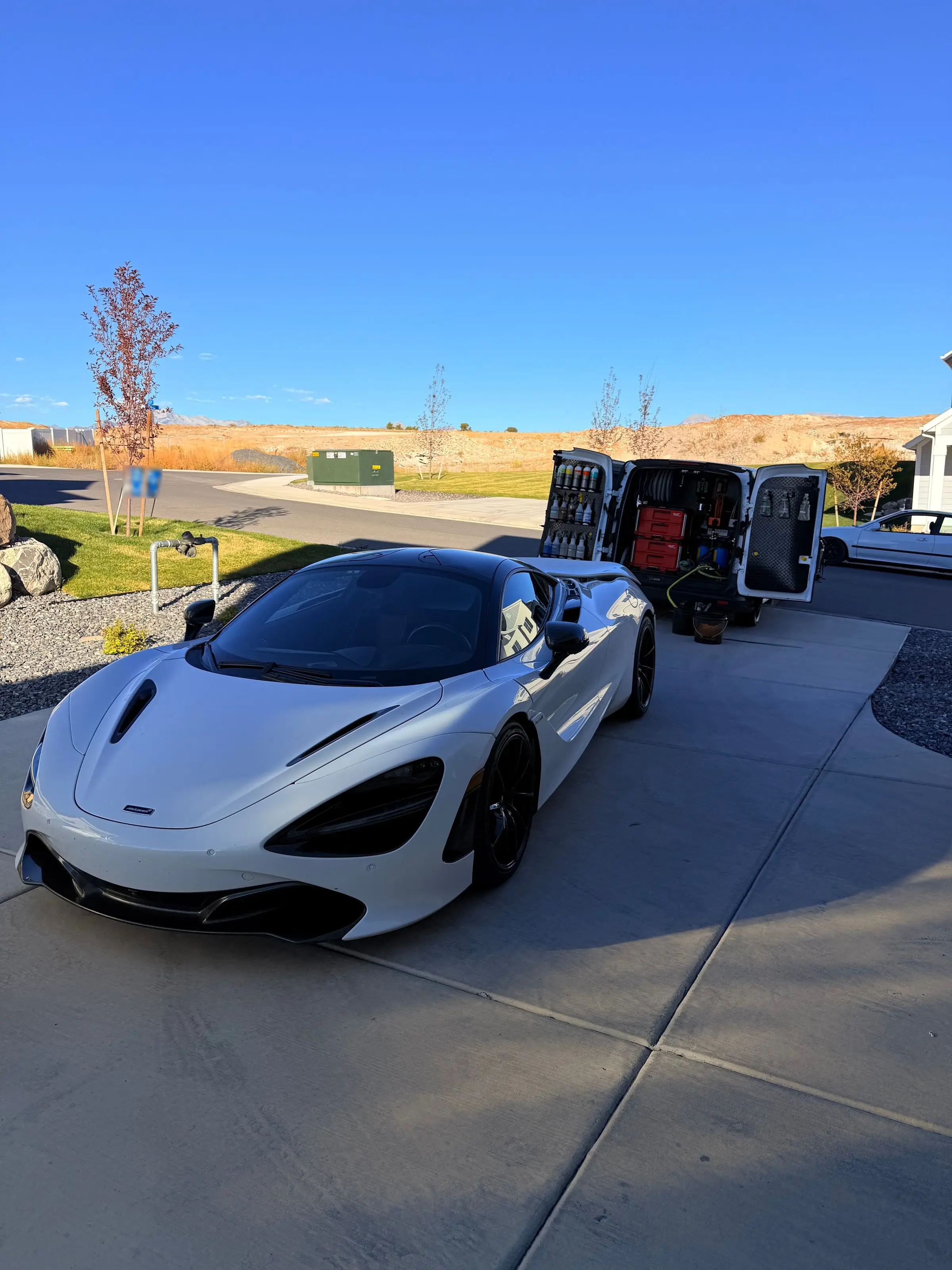 A white McLaren 720S in a driveway beside the open Trey's Detailing van