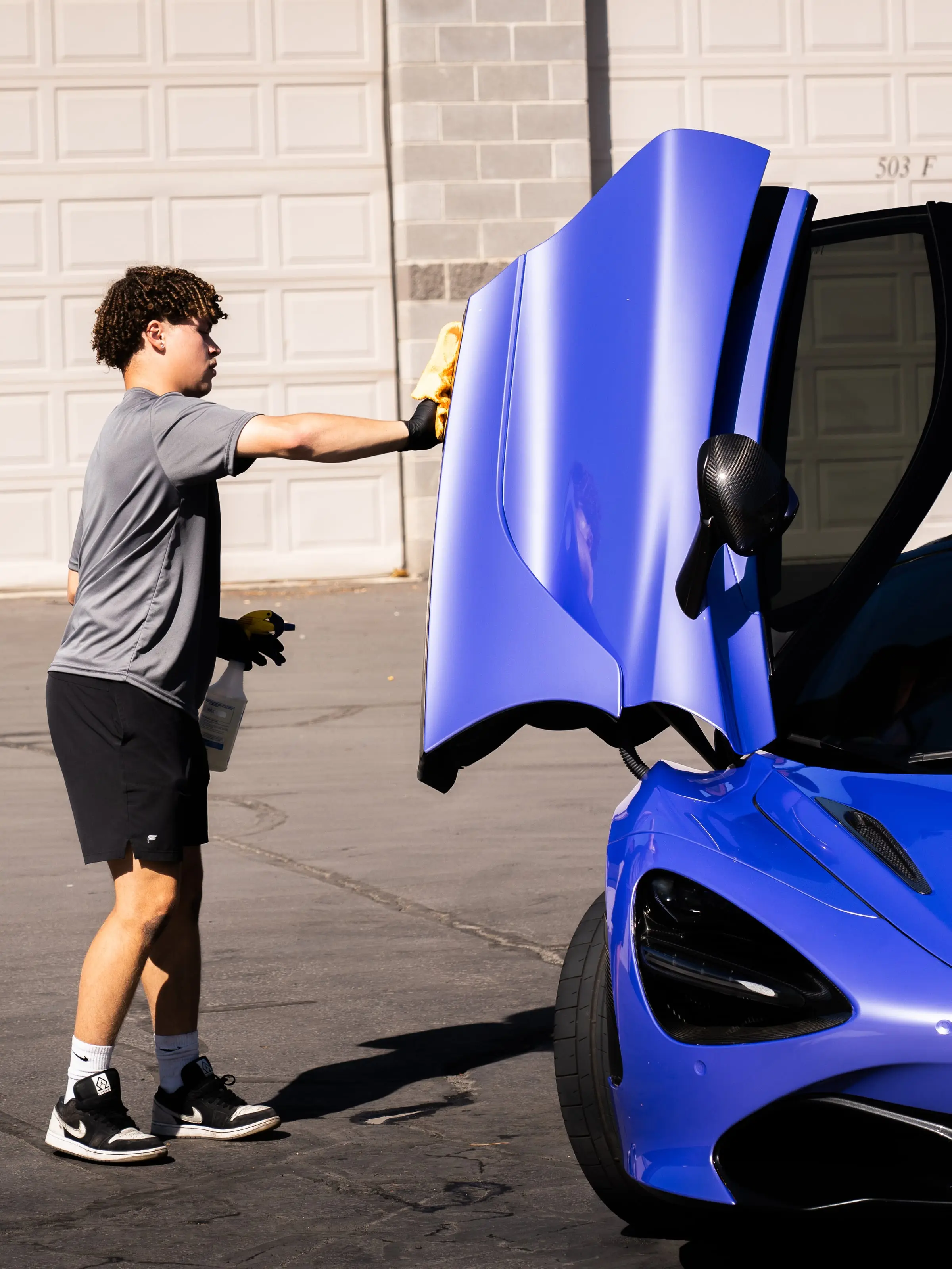 A blue McLaren 720S with a dihedral door raised, being wiped down outside the shop