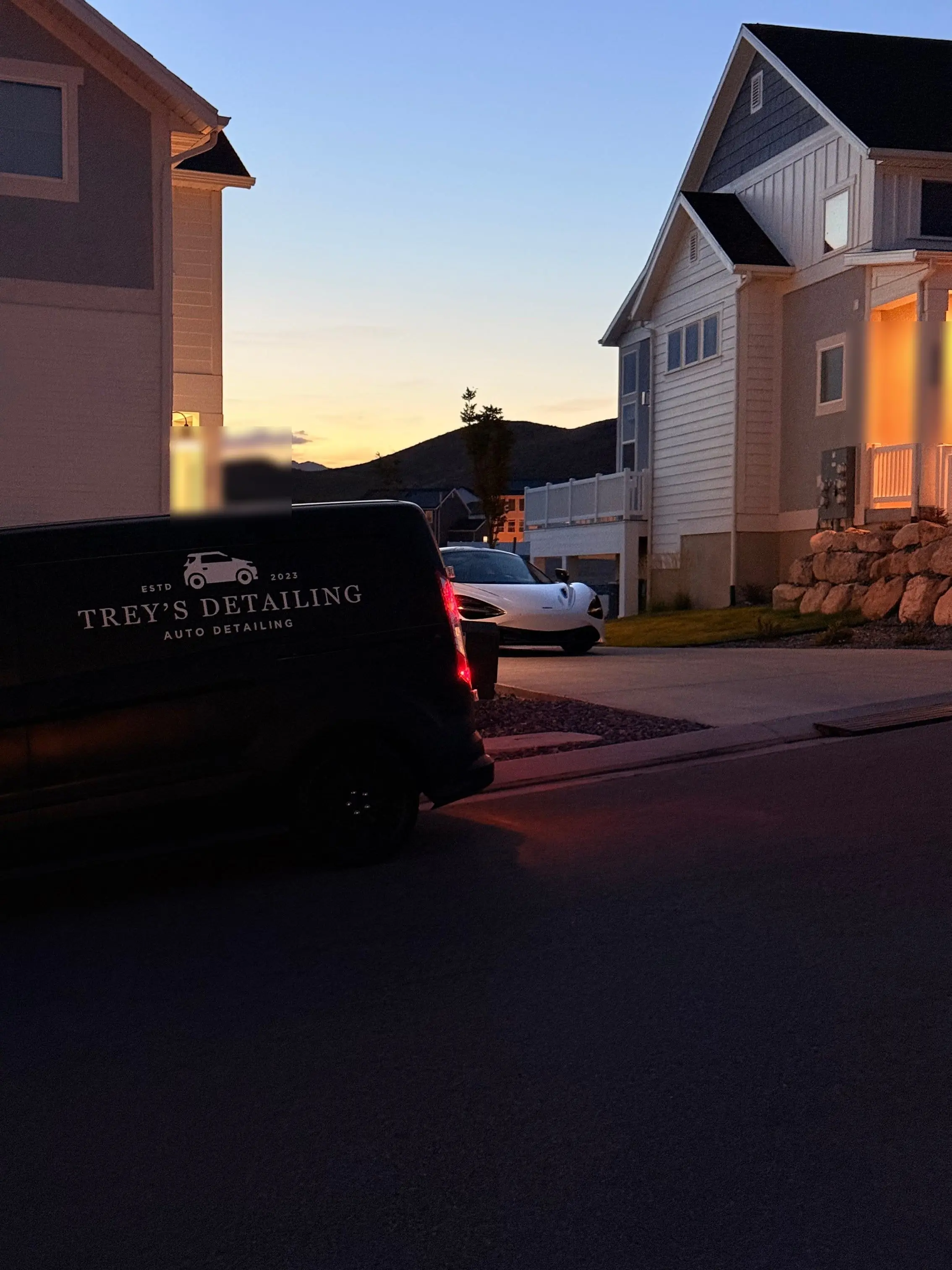 The Trey’s Detailing logo on a dark vehicle at dusk, a white McLaren parked beyond