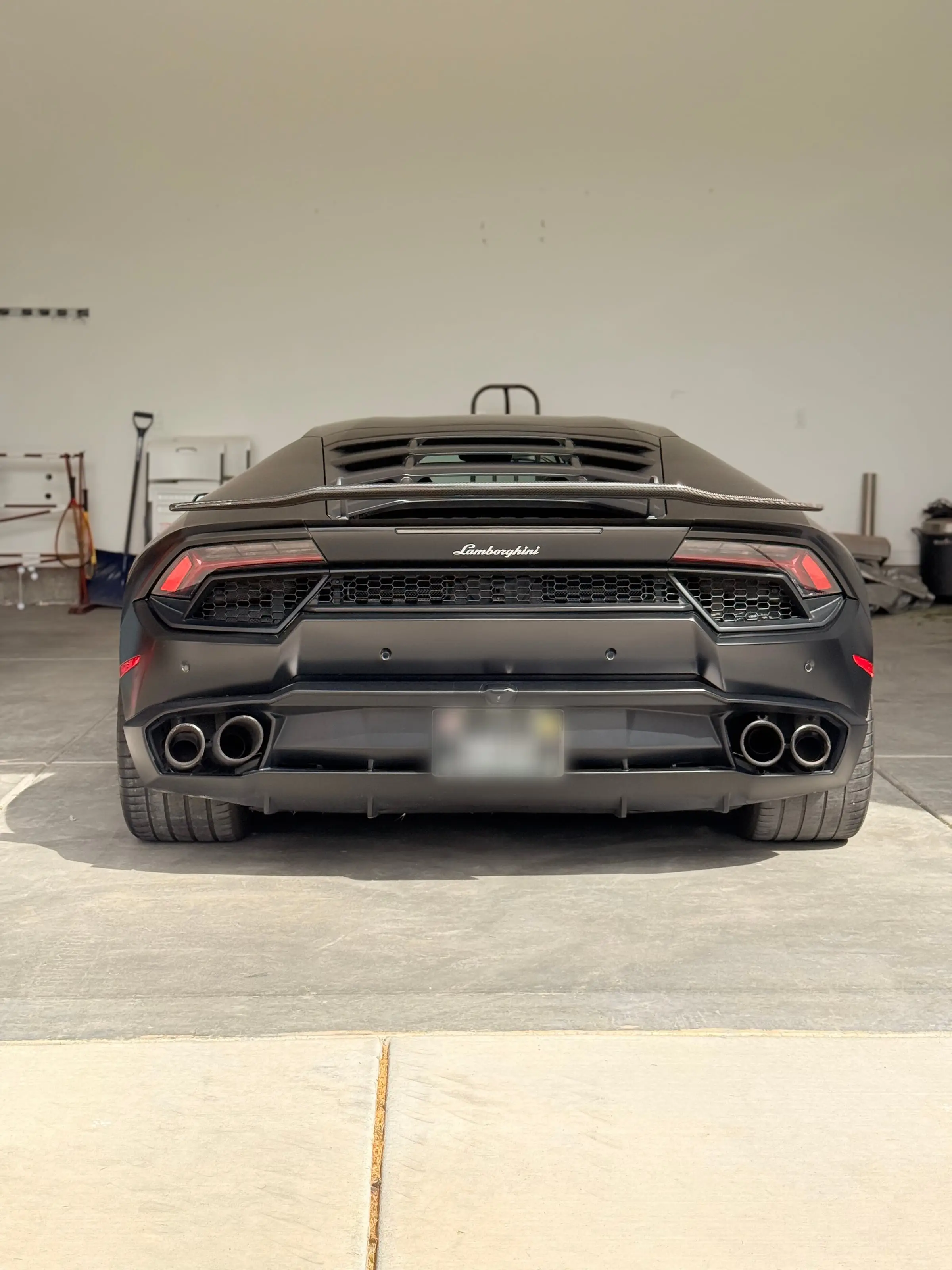 The rear wing and quad exhausts of a dark Lamborghini Huracán in the shop