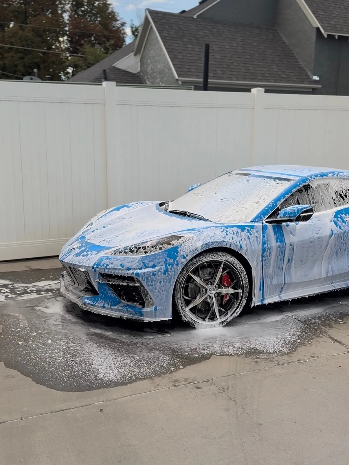 A blue Corvette C8 covered in snow foam in a driveway
