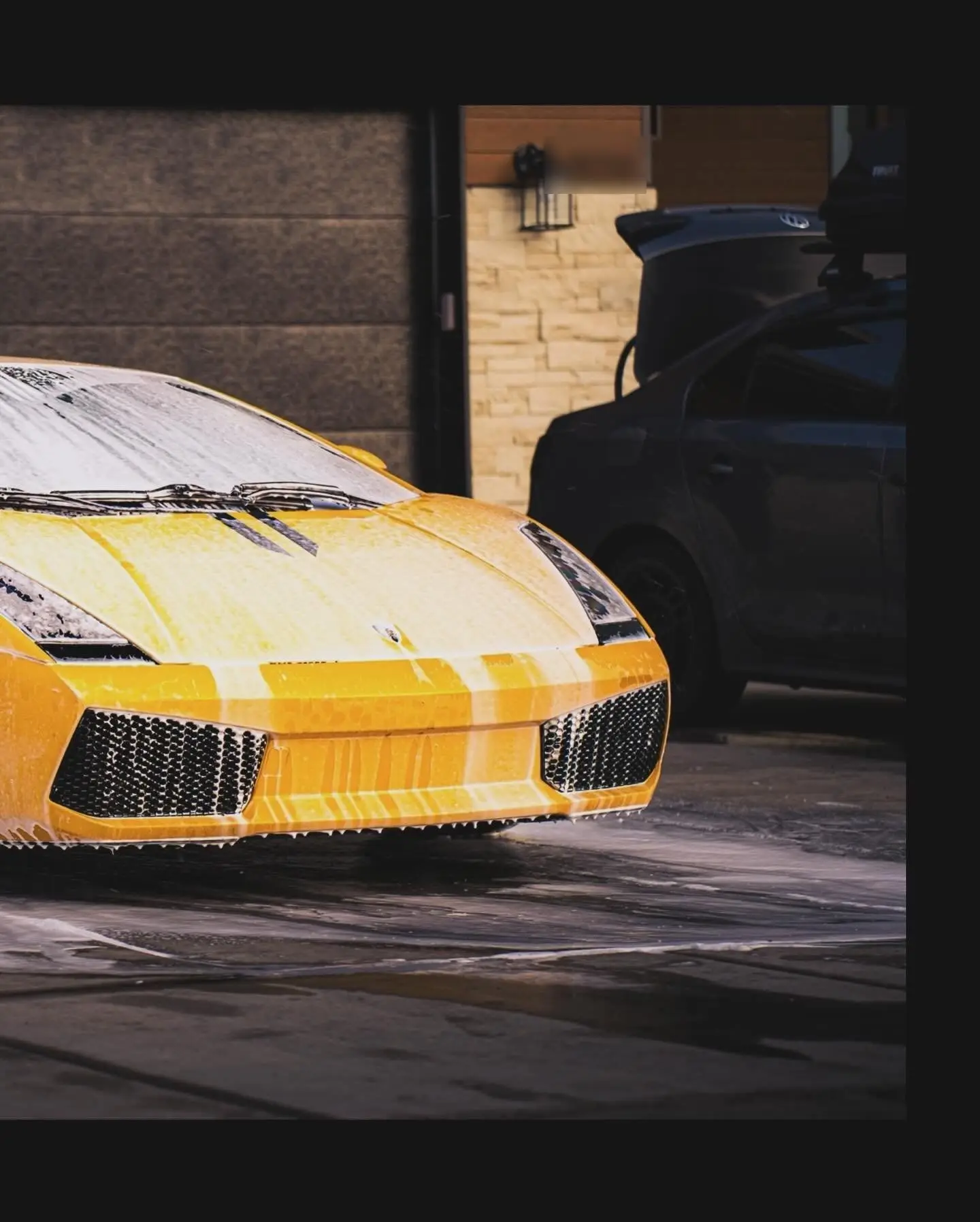 A yellow Lamborghini Gallardo covered in foam outside a garage at dusk