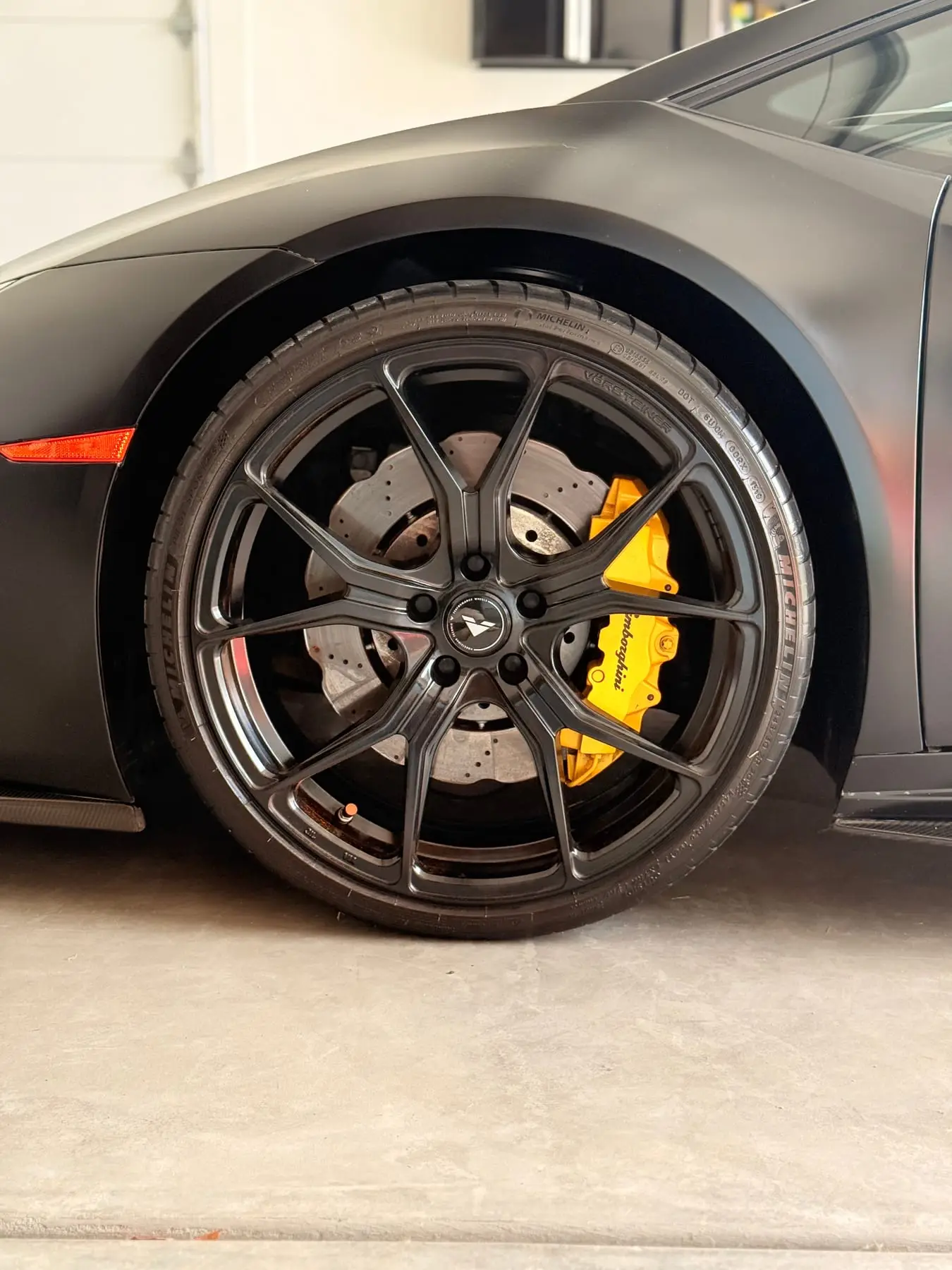 A yellow Lamborghini brake caliper behind the dark wheel of a Huracán