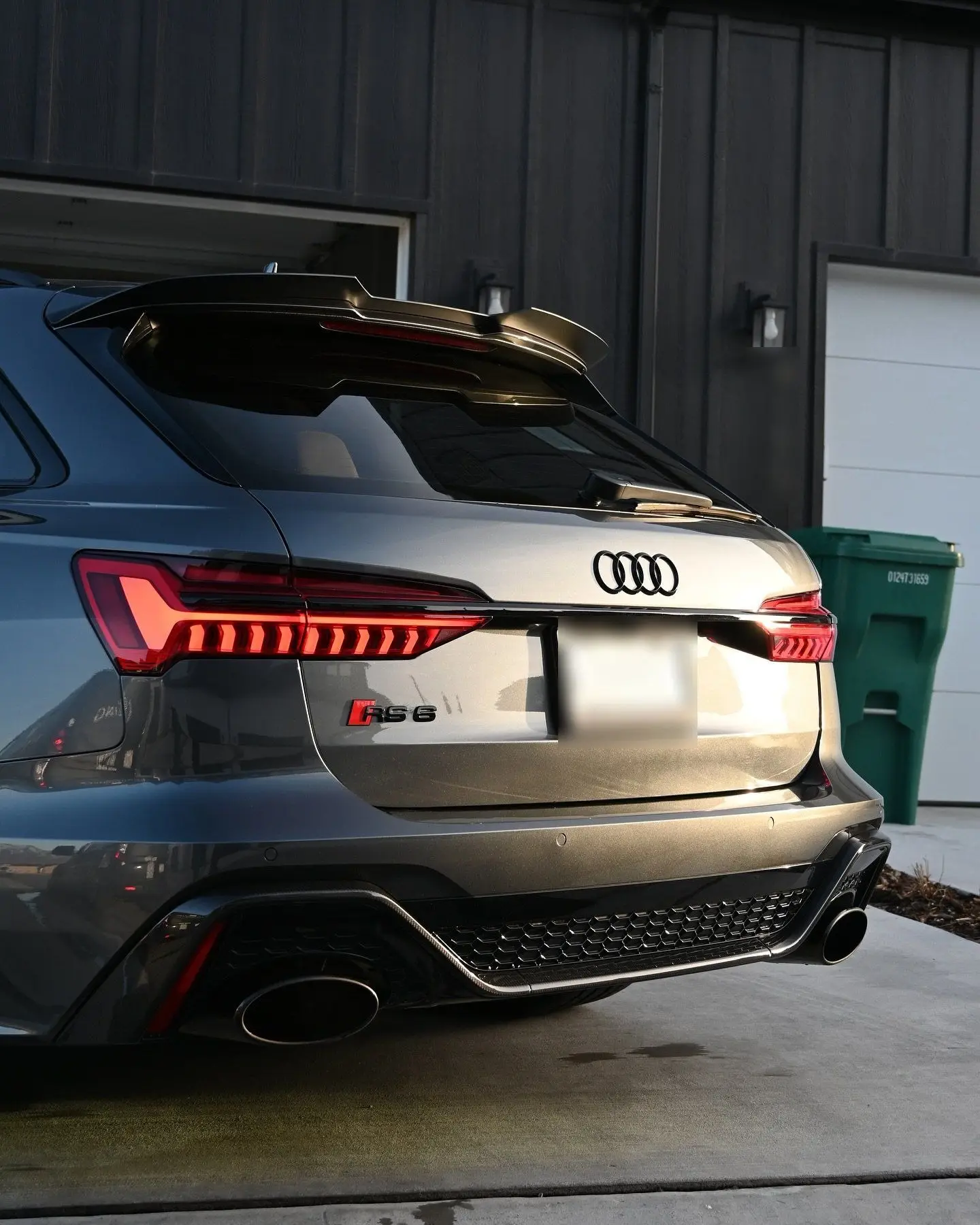 The rear of a gray Audi RS6 with taillights lit outside a dark garage