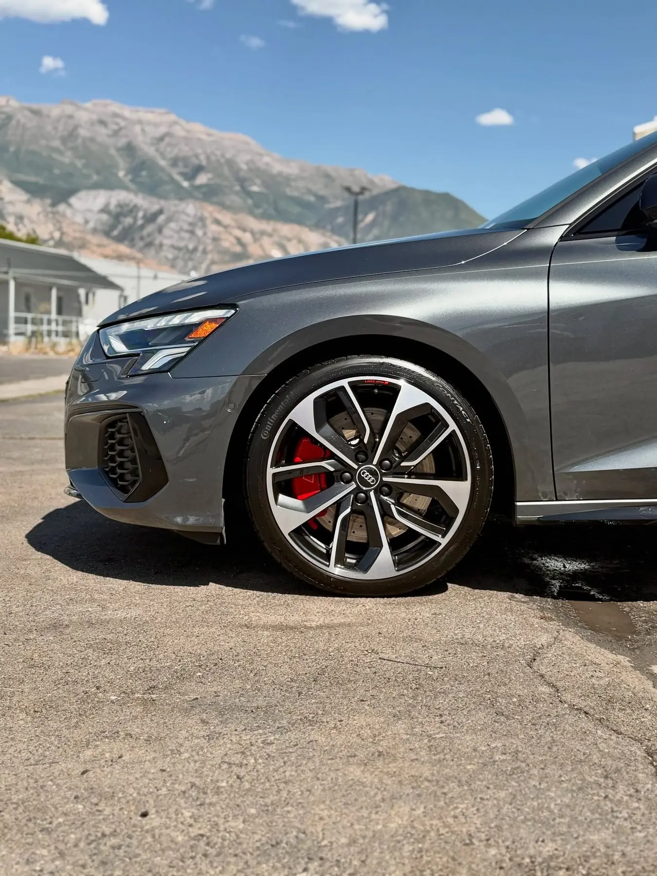 A gray Audi S3 with red calipers, mountains behind