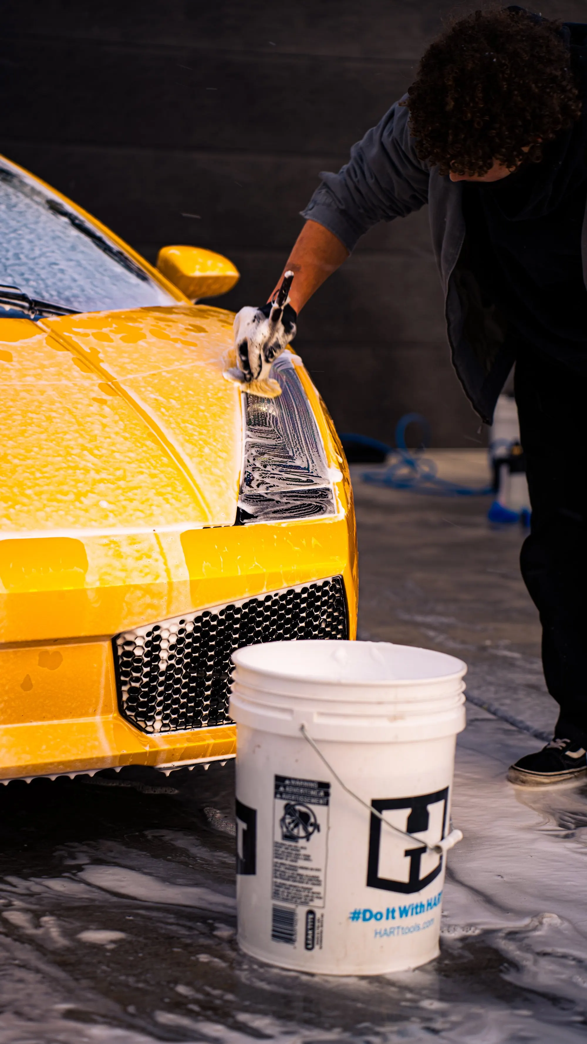 A technician washing the hood of a yellow Lamborghini, wash bucket in frame