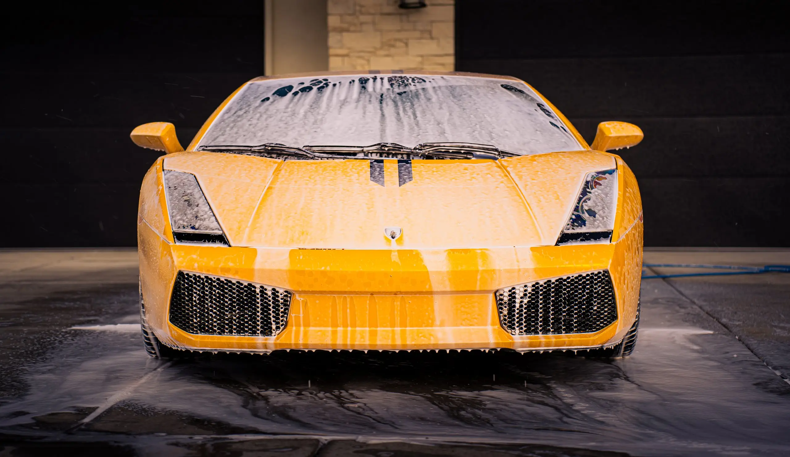 A yellow Lamborghini Gallardo head-on in the Trey's Detailing bay, hood covered in wash foam