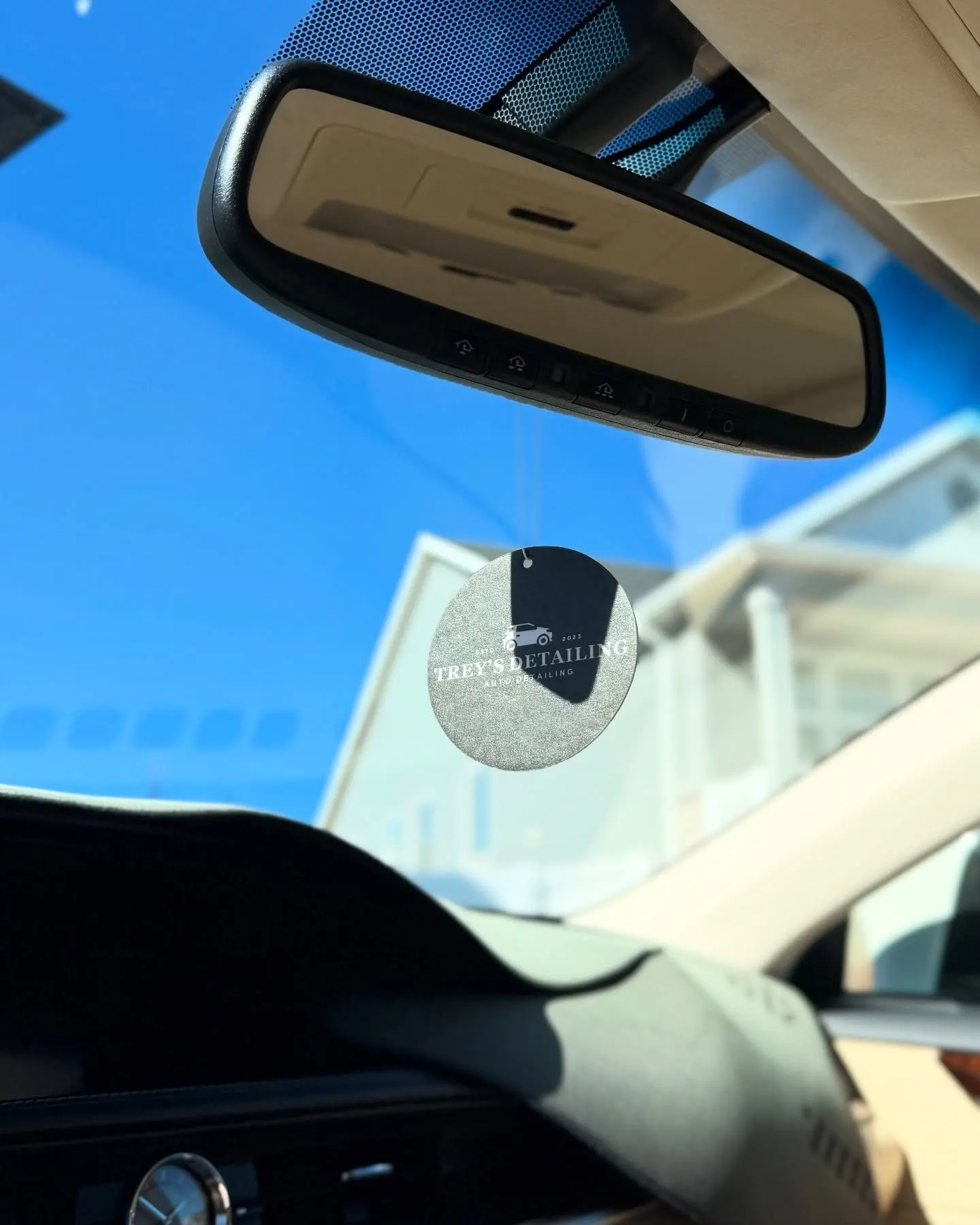 The windshield and mirror from inside the car, sky visible through the glass